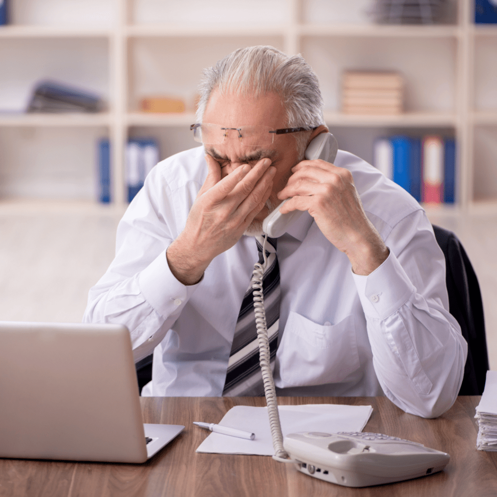 Stressed elderly man in an office holding a business phone, representing benefits of phone business service and VoIP support to businesses