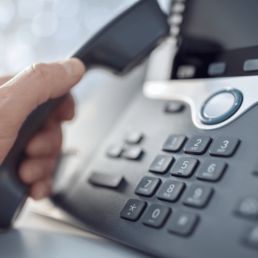 Hand lifting the receiver of a modern office business phone used for VoIP services and business communication